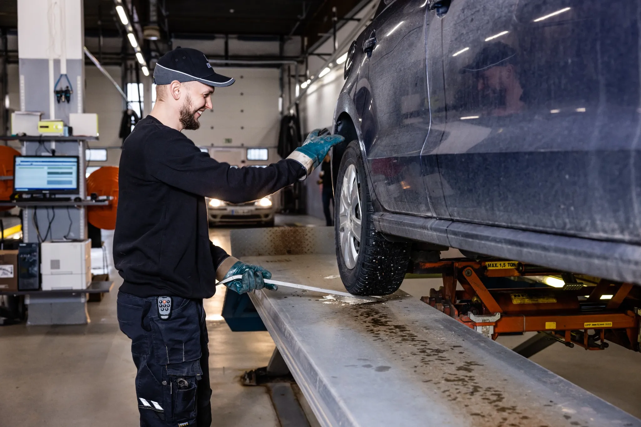 Katsastaja tarkastaa nosturilla olevan auton rengasta ja jousitusta, varmistaen ajoneuvon turvallisuuden ja toimivuuden.