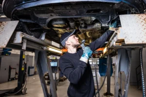 DEKRAn katsastaja tarkastaa auton alustaa hydraulisella nosturilla, käyttäen käsivalaisinta mahdollisten ongelmien havaitsemiseksi katsastuksen aikana.
