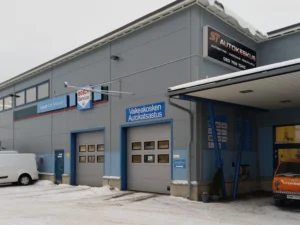 DEKRA Katsastus Valkeakosken halli ulkoa kuvattuna, jossa ovi ajoneuvoilla ja sen yläpuolella on DEKRA Katsastus-kyltti.
